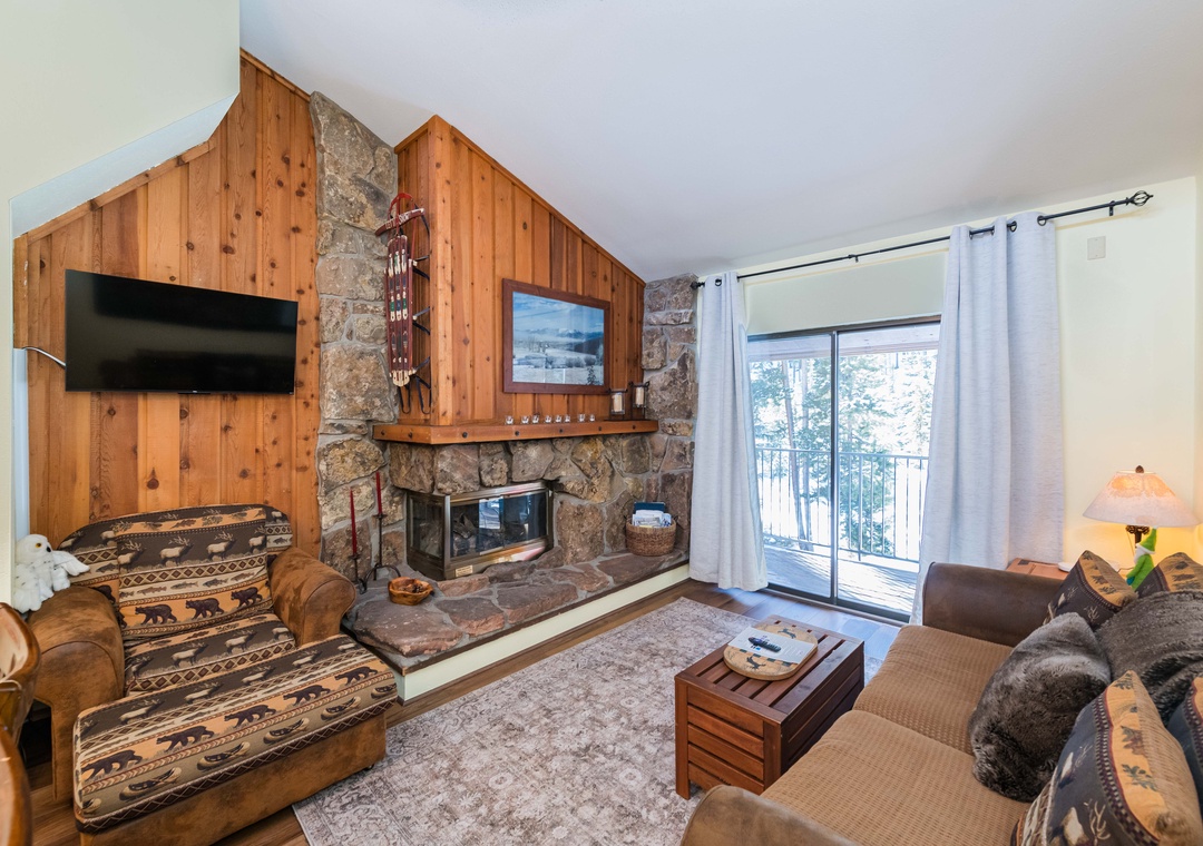 Cozy up by your stone fireplace while enjoying mountain views from the balcony in this rustic living room.