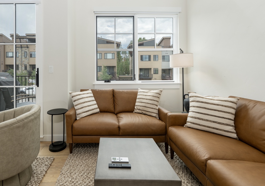 Sink into luxurious leather sofas in your bright living space, where large windows frame peaceful neighborhood views and modern comfort awaits.