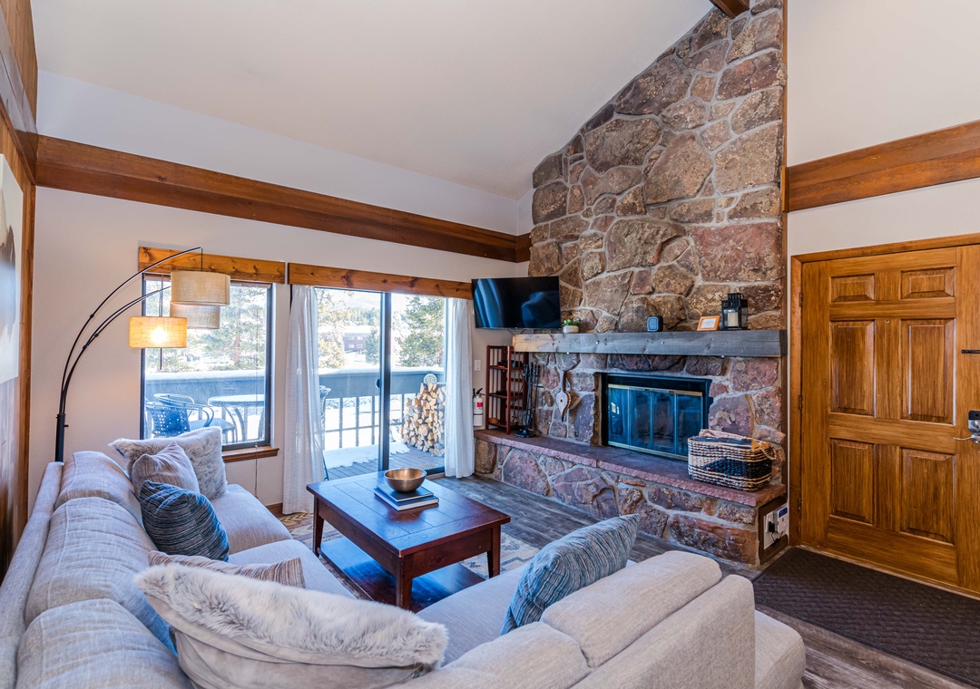 Cozy up by your stone fireplace in this warm living room, where rustic beams and soft seating create the perfect mountain retreat atmosphere.