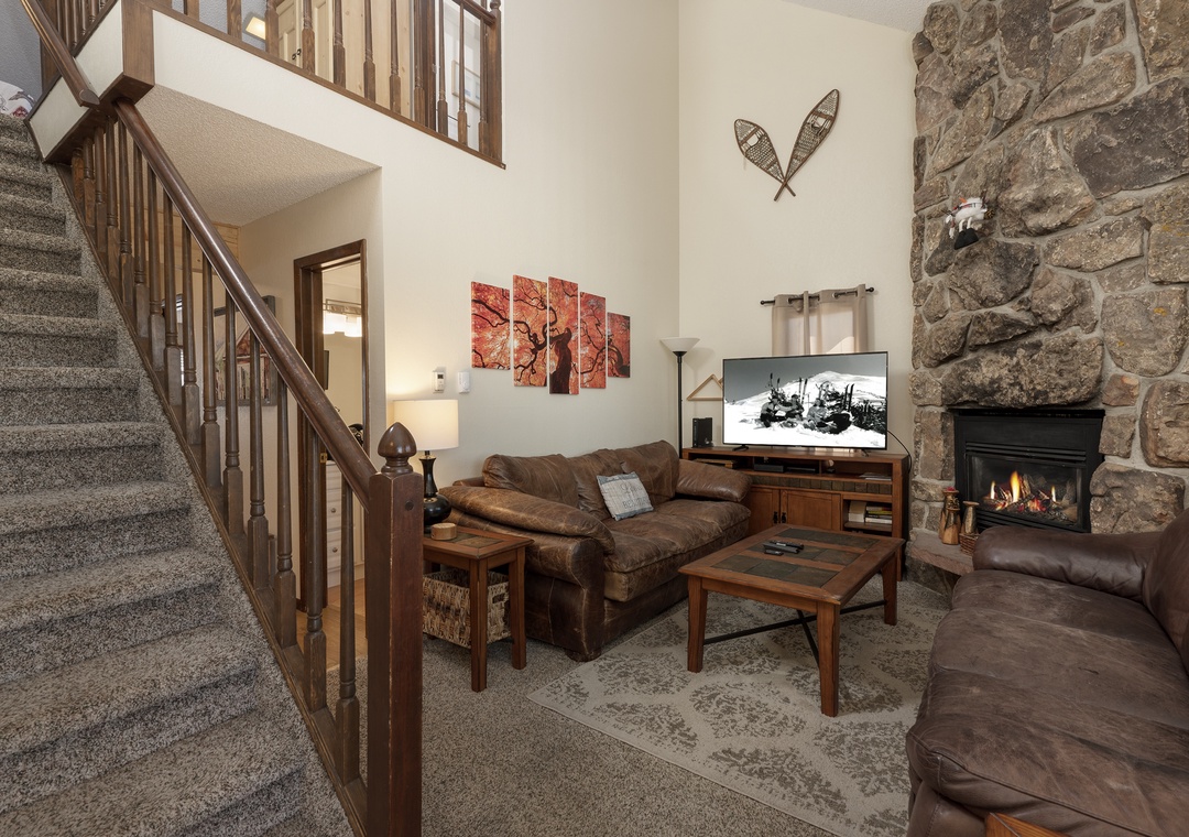 Cozy up in your spacious living room with warm leather seating, crackling stone fireplace, and rustic mountain charm perfect for relaxing evenings.