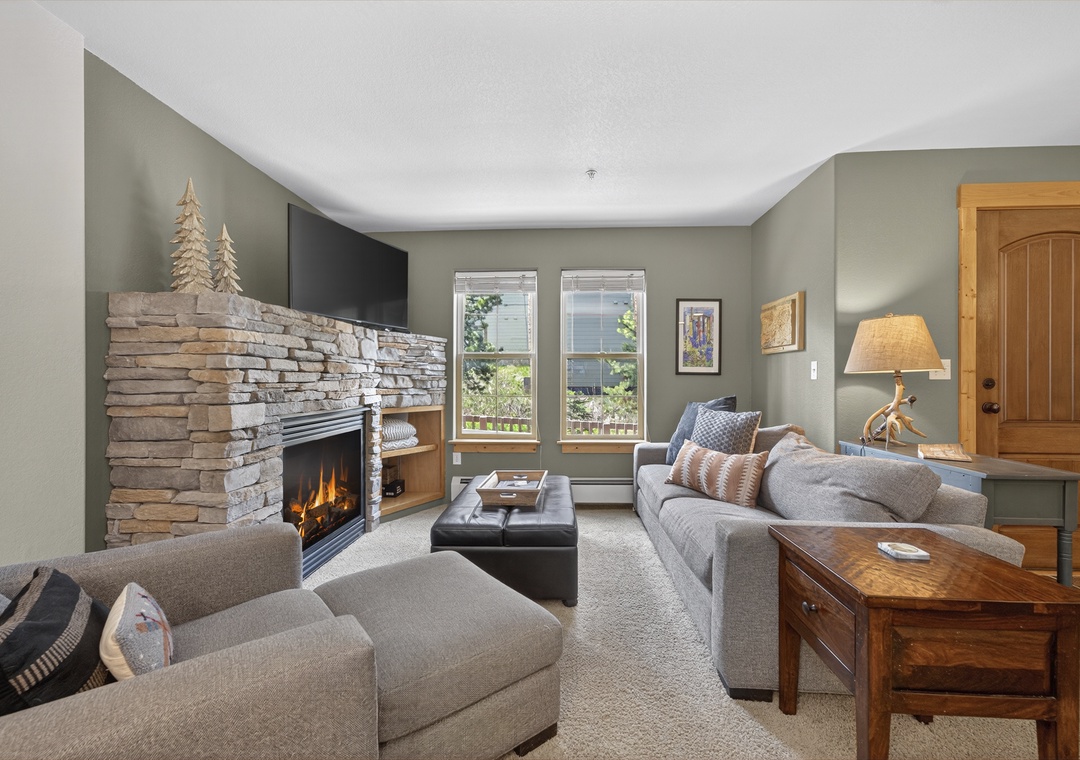 Unwind in your serene living room, where a crackling stone fireplace and plush seating create the perfect mountain retreat after a day of adventure.