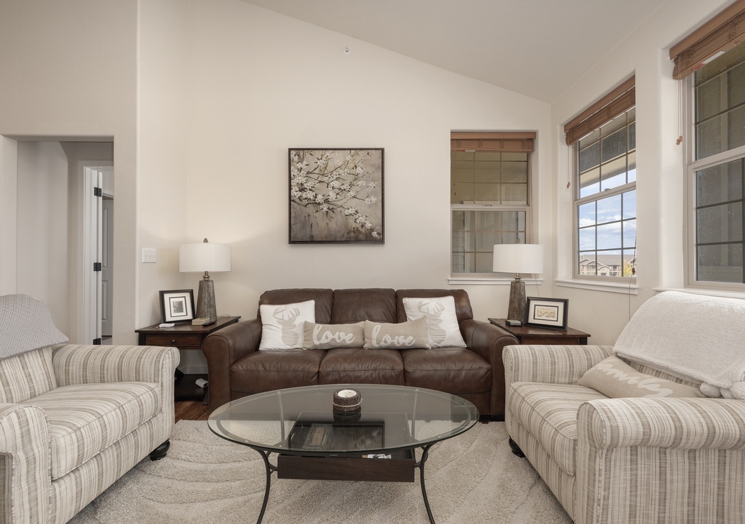 Sink into plush seating around your glass coffee table, where love-themed pillows invite cozy conversations in this bright, welcoming living space.