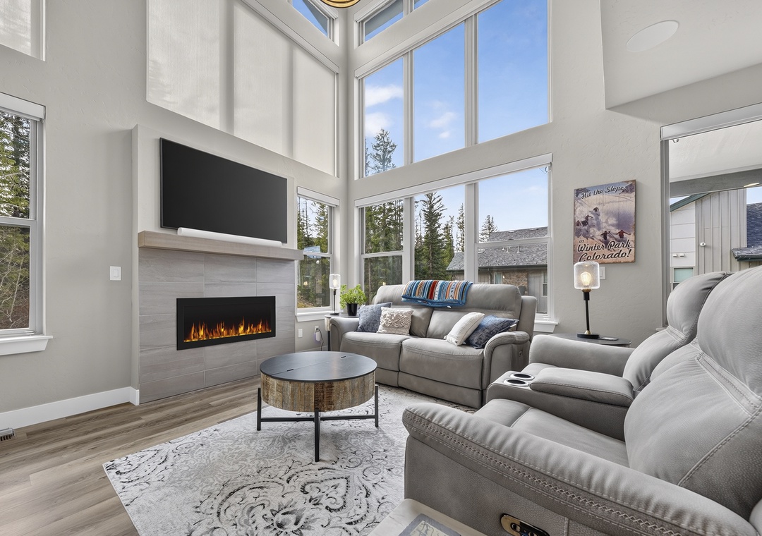 Sunlight floods through soaring windows, warming your cozy living space where the modern fireplace creates a perfect gathering spot for mountain evenings.