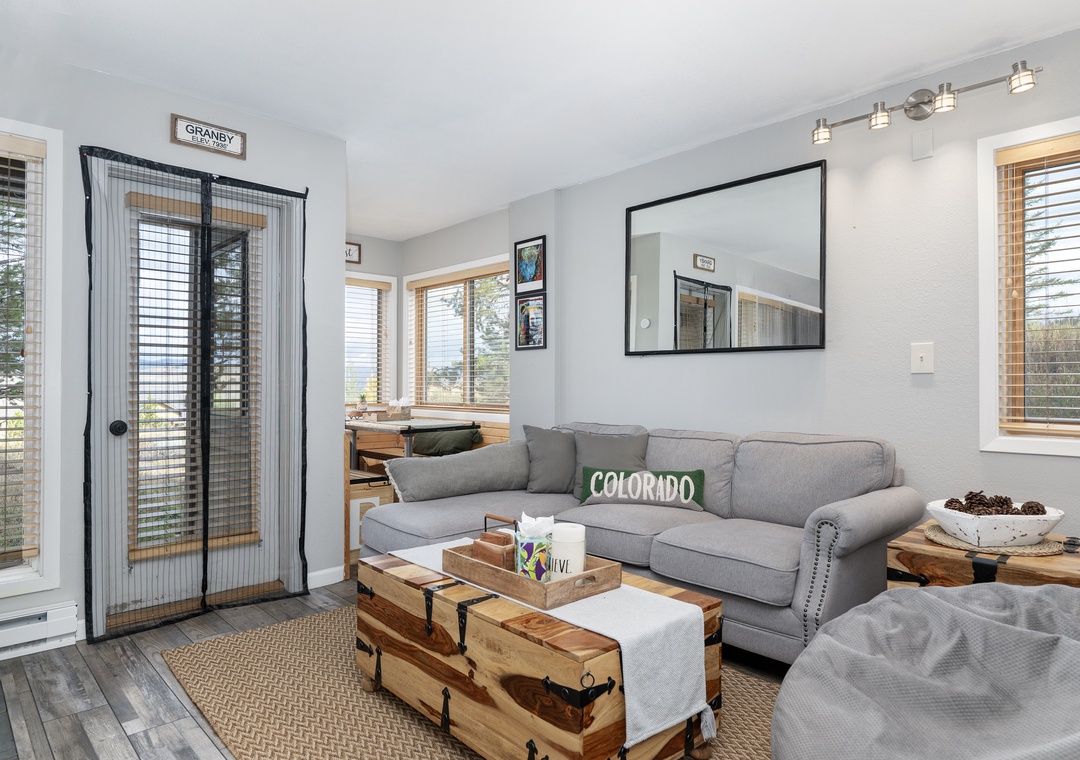 Unwind in your bright living space with plush gray seating, natural wood accents, and windows that frame peaceful views.
