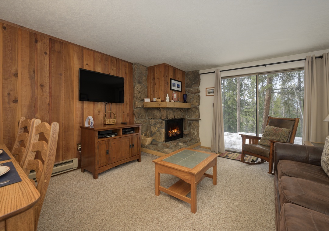 Unwind by your crackling fireplace with mountain views streaming through large windows in this cozy wood-paneled living room.