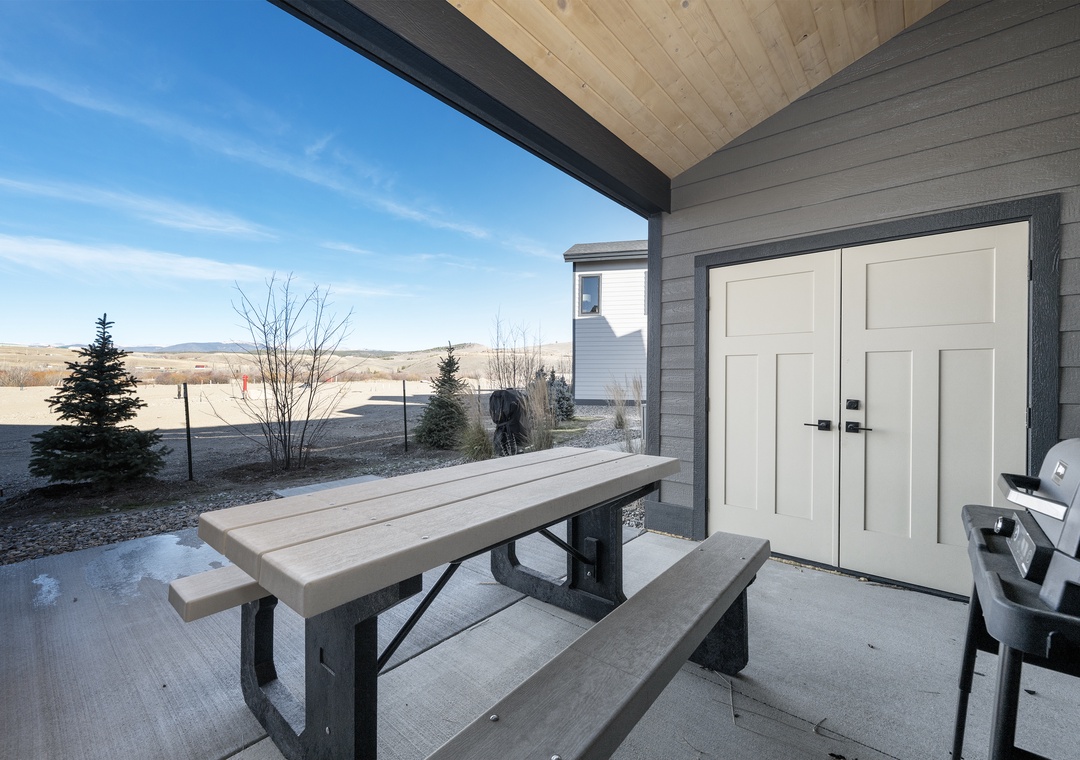 Your covered patio invites outdoor dining with a rustic picnic table and grill, perfect for prairie sunset barbecues.