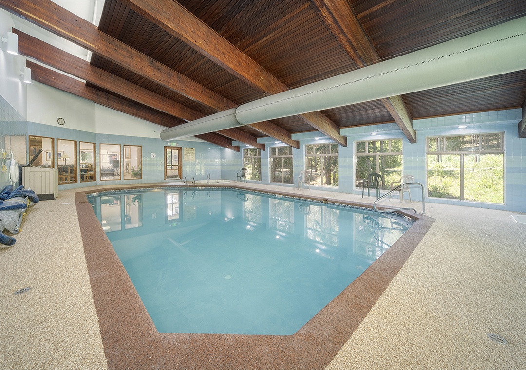 Dive into the clubhouse indoor pool beneath stunning exposed wood beams, where natural light pours through windows overlooking the surrounding trees and greenery.