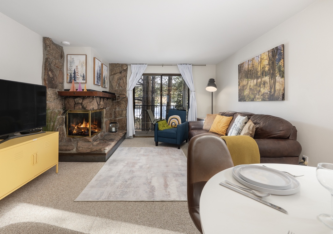 Unwind in your cozy living space with a crackling stone fireplace, plush leather sofa, and peaceful forest views from your private balcony.