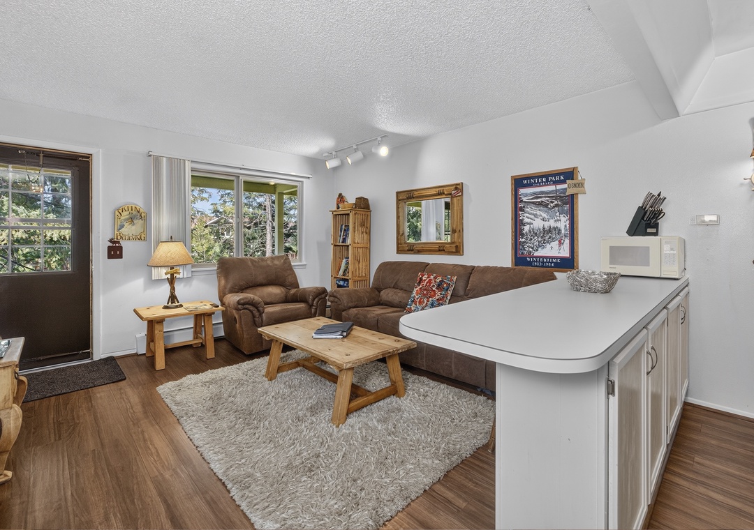 Step into your comfortable mountain retreat where warm wood tones and cozy furnishings welcome you home. Natural light pours through large windows framing tree-lined views, inviting you to relax in this inviting space.