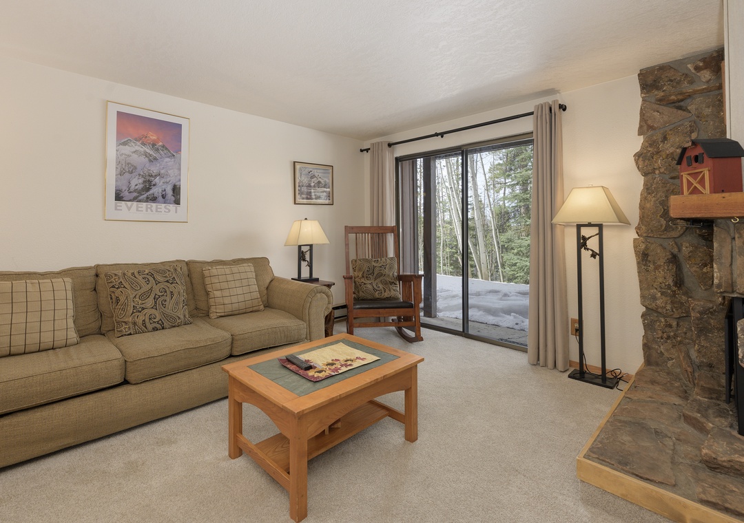 Unwind in your cozy living room with a crackling stone fireplace and private patio access to snowy surroundings.