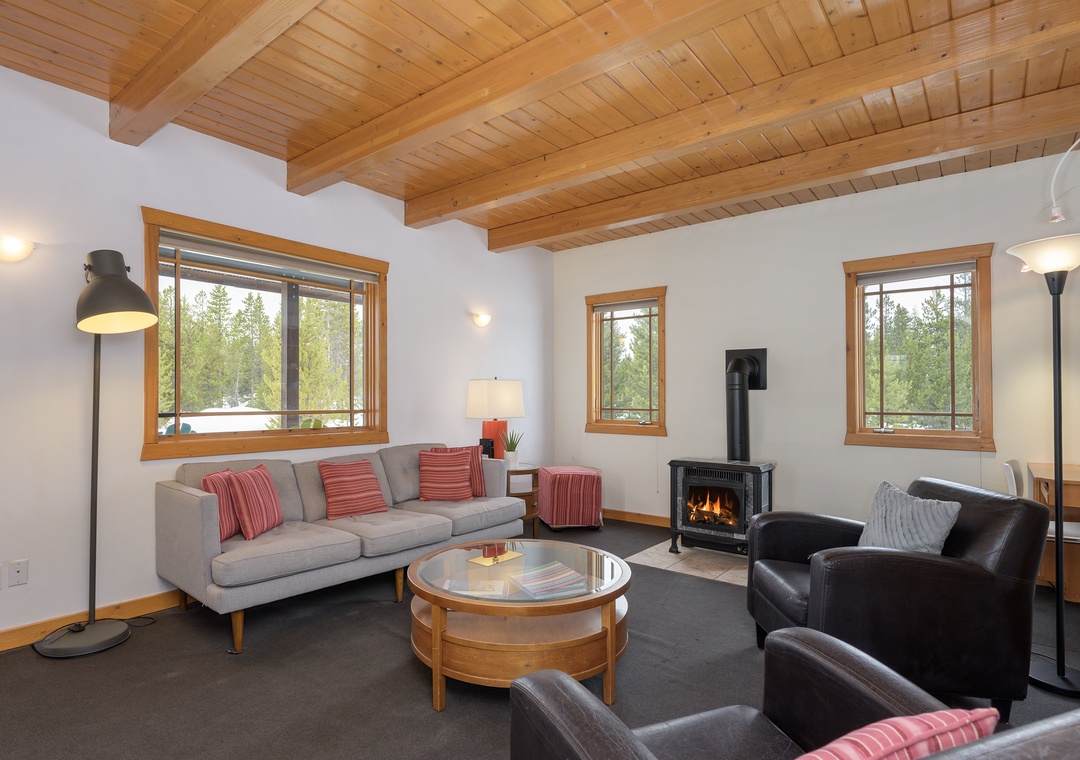 Unwind in your spacious living room with exposed beam ceilings, cozy fireplace, and forest views through large windows.