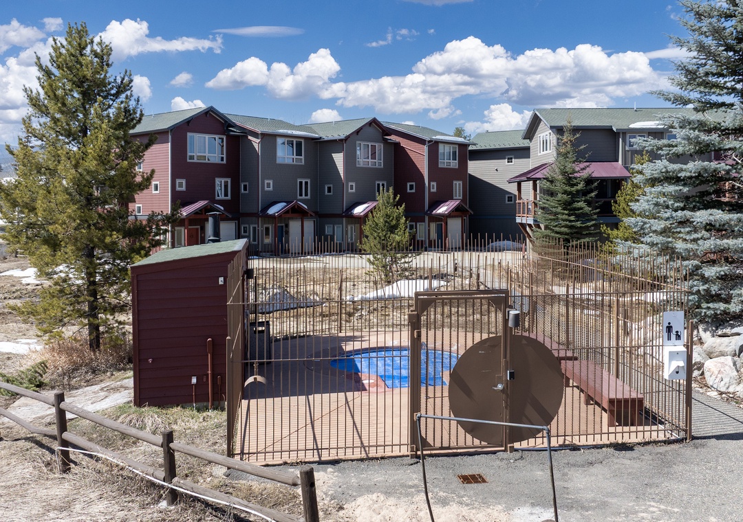 Mountain vacation rental complex featuring townhomes with fenced pool area surrounded by mature evergreen trees.