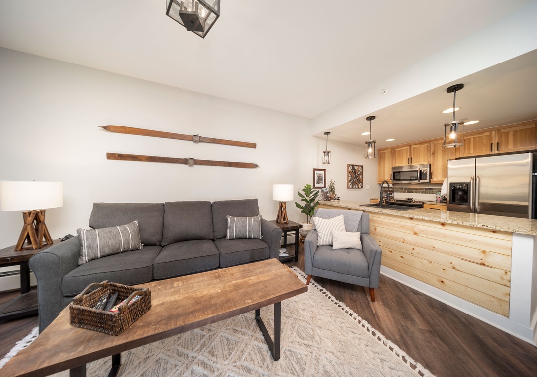 Unwind in your inviting living space with soft seating and mountain-inspired décor, flowing seamlessly into a fully-equipped kitchen perfect for preparing meals together.