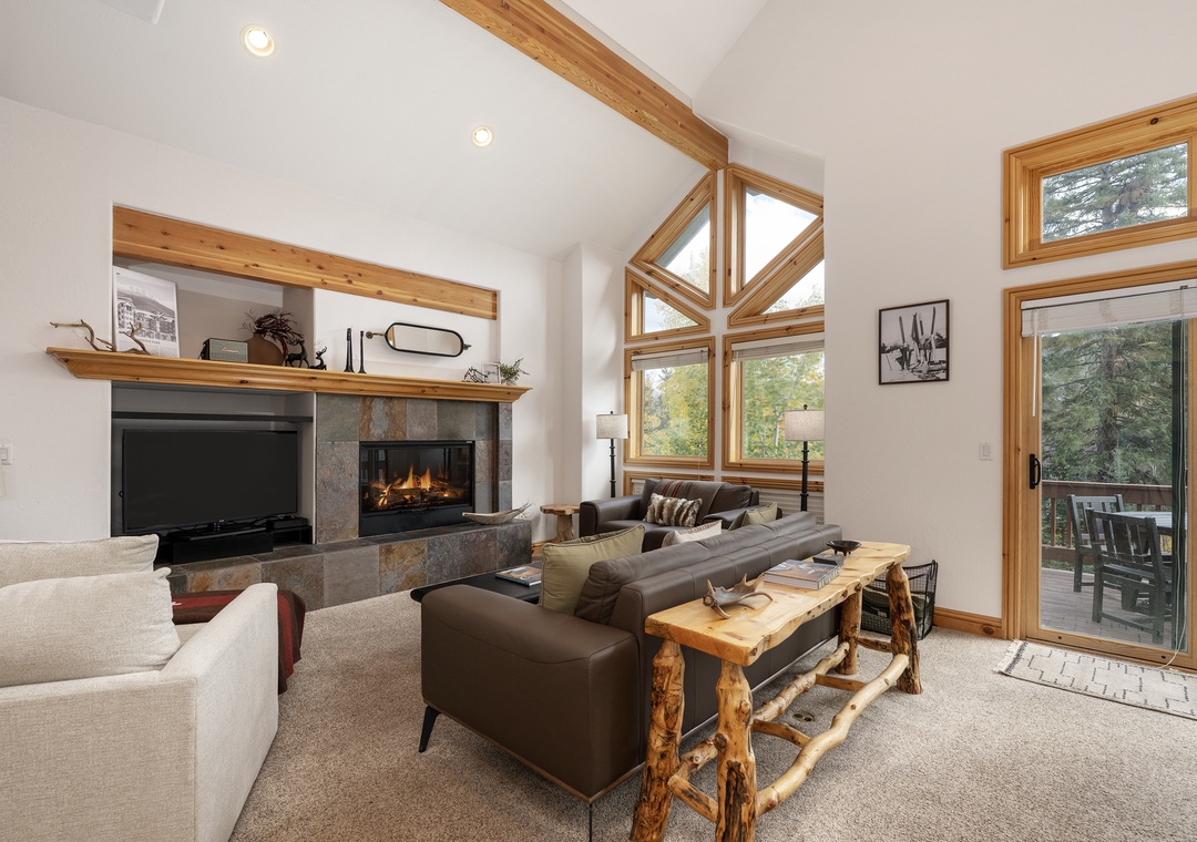 Relax in your spacious living room featuring soaring ceilings, a cozy fireplace, and floor-to-ceiling windows that flood the space with natural light.