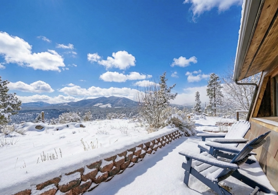 Winter mountain views stretch endlessly from this snow-covered deck, where Adirondack chairs await warmer days amid pristine alpine scenery.