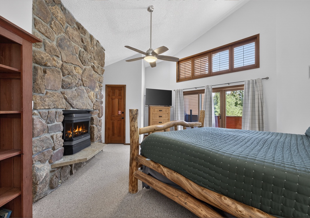 Unwind in your cozy mountain retreat with a roaring stone fireplace, rustic log-framed bed, and peaceful views. High ceilings and natural light create the perfect escape for restful nights.