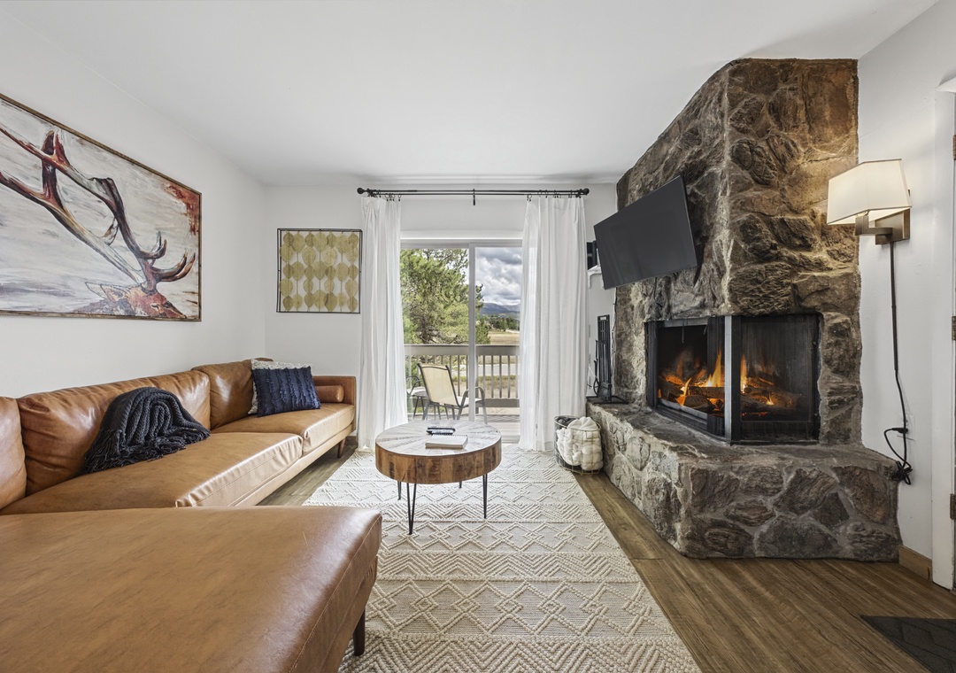 Unwind on plush leather seating in your bright living room, where a rustic stone fireplace radiates warmth and sliding doors open to your private balcony with peaceful outdoor views.