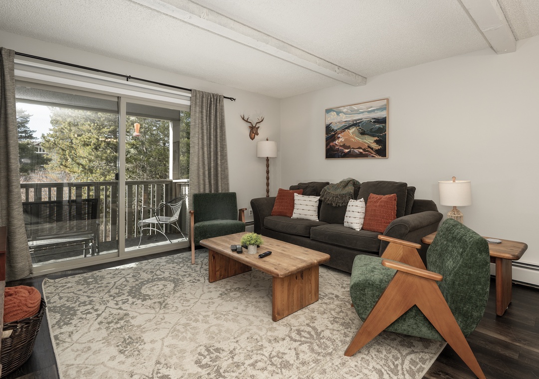 Relax in your cozy living room with rustic charm, featuring a plush sofa and warm wood accents overlooking peaceful treetops from your private balcony.