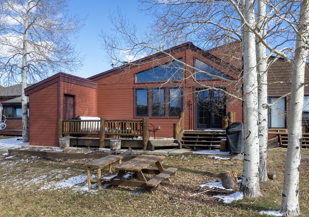 Mountain lodge surrounded by pristine aspen trees and scenic winter landscape, featuring wooden deck and picnic area.