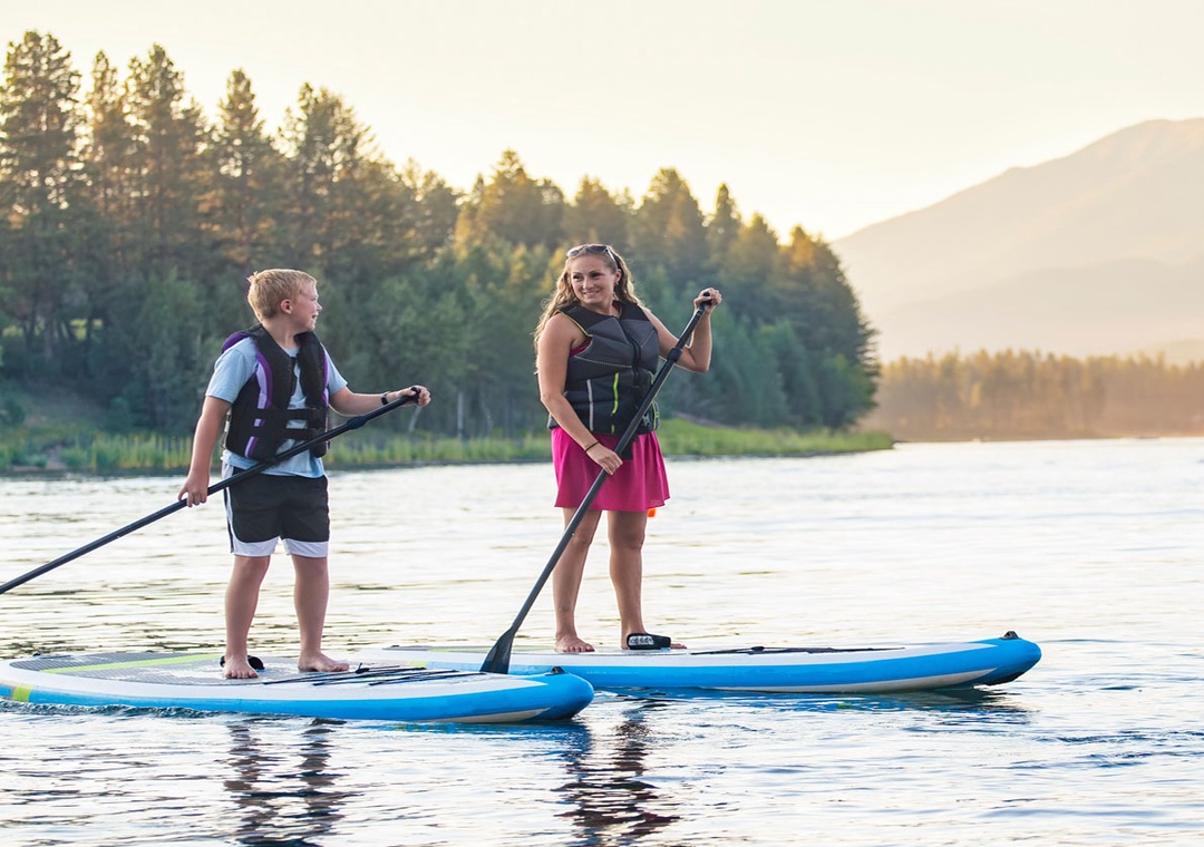 Paddleboard adventure on pristine mountain lake during your stay at Soda Springs Ranch condo 3C, surrounded by peaceful forest and distant peaks.