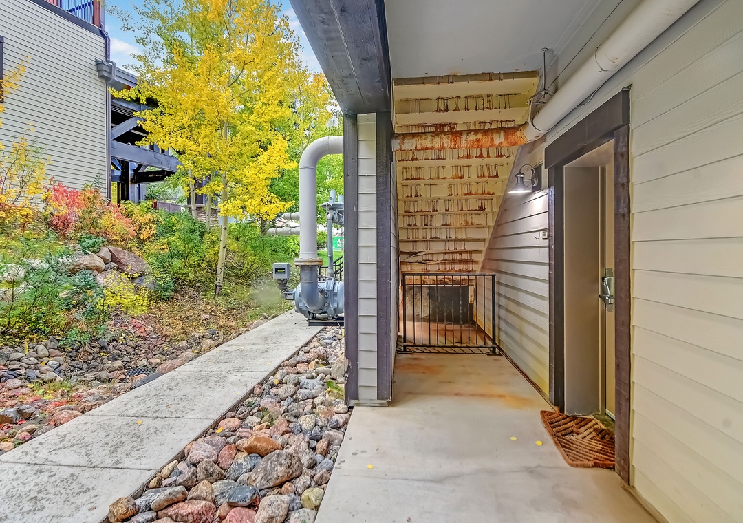 Covered entryway with convenient access to laundry facilities, set against landscaped gardens showcasing vibrant autumn foliage and nearby mountain homes.
