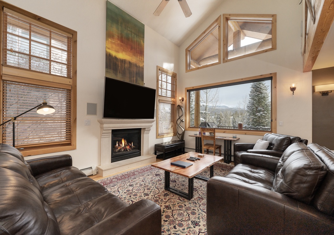 Cozy up in your spacious living room with leather seating, crackling fireplace, and stunning mountain views through floor-to-ceiling windows.