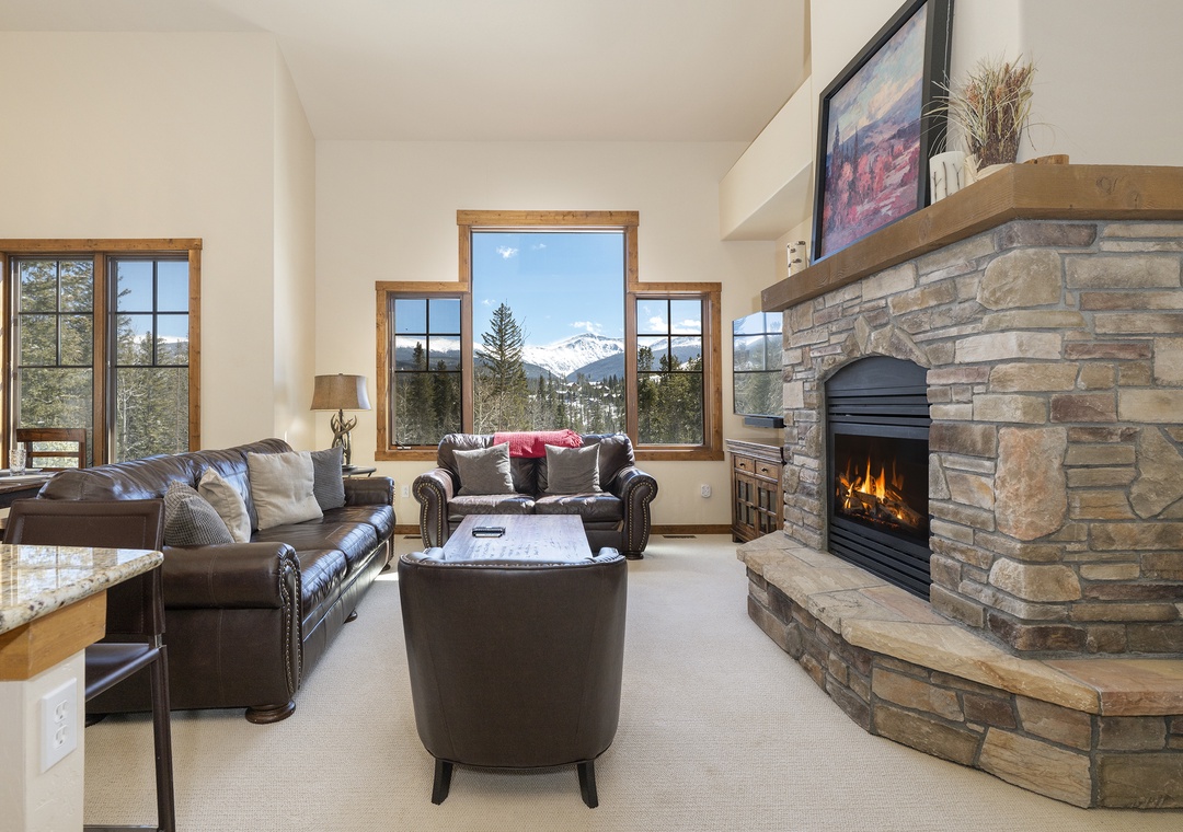 Cozy up by your stone fireplace while soaking in stunning mountain views through floor-to-ceiling windows in this inviting living space.