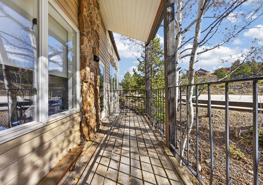 Step onto your private deck, where rustic wood posts meet dappled sunlight and peaceful outdoor living awaits beneath a charming covered roof.