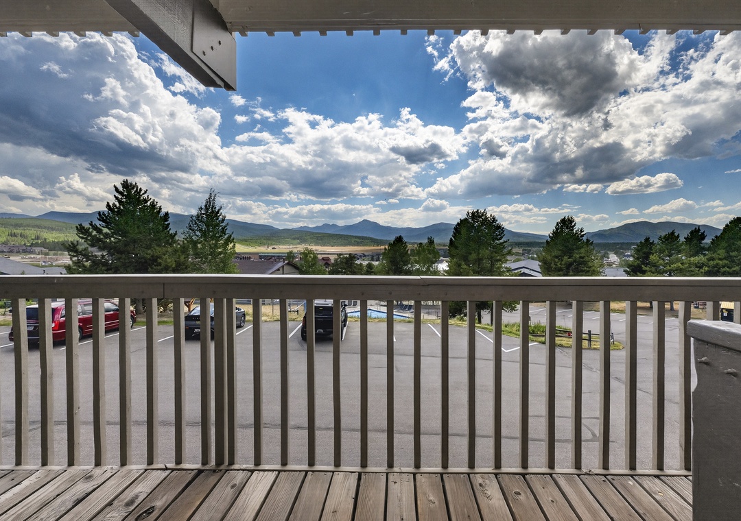 A balcony view capturing mountain ranges and expansive sky, with parking and local surroundings visible below—part of the area surrounding your arrival.