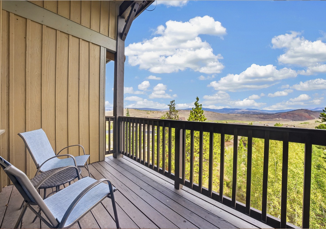 Sweeping views of rolling hills and open skies stretch before a private balcony, where comfortable chairs invite you to relax and soak in the quiet beauty of the surrounding landscape.