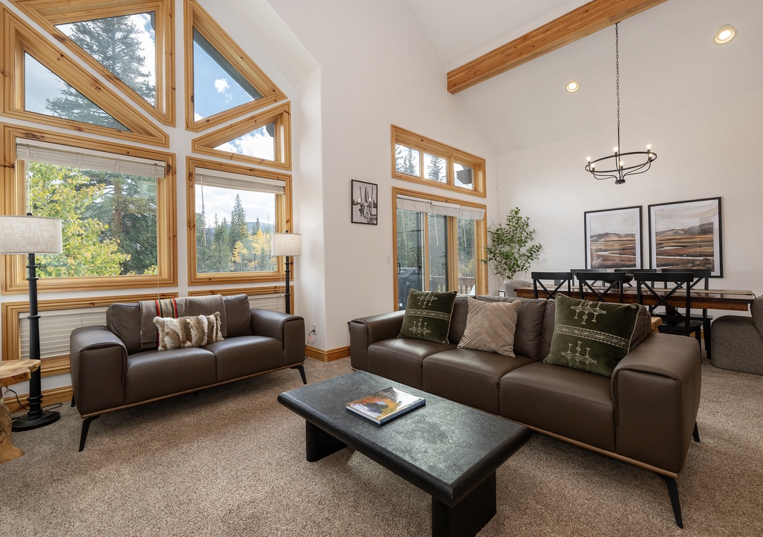 Unwind in your bright living space with soaring ceilings, warm wood beams, and windows framing stunning forest views.
