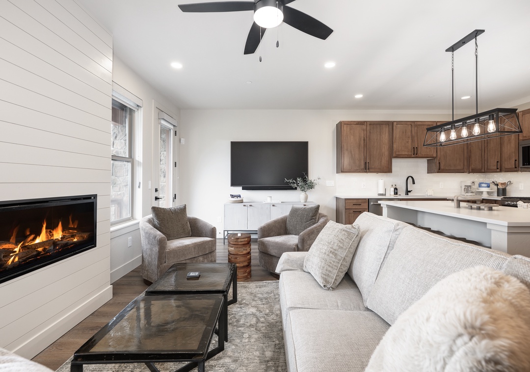 Unwind in your cozy living space where modern elegance meets comfort—crackling fireplace, plush seating, and open kitchen create the perfect retreat.