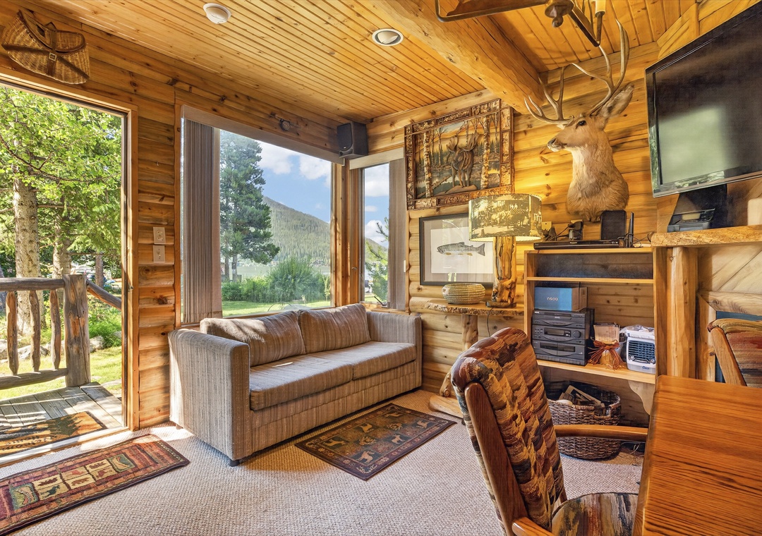 Relax in your rustic cabin retreat where warm wood paneling, cozy seating, and large windows frame stunning mountain views. Step outside to the deck and breathe in the fresh alpine air.