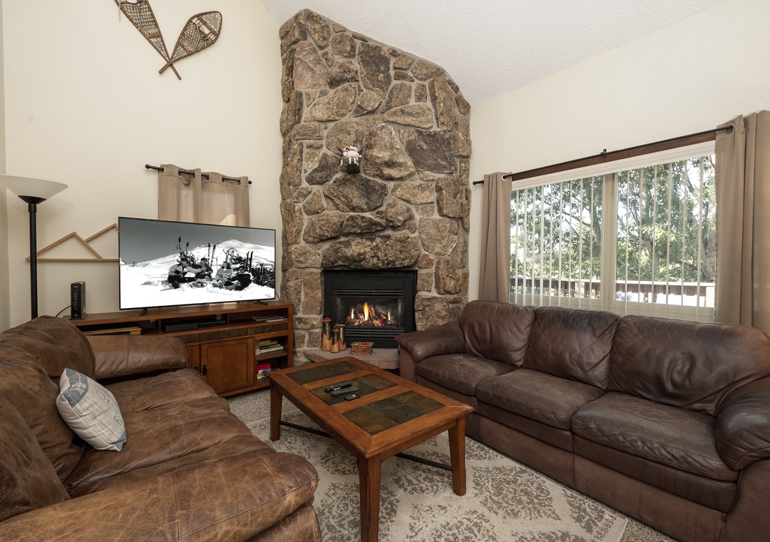Unwind in your cozy living room with leather seating, stone fireplace, and mountain views through large windows.