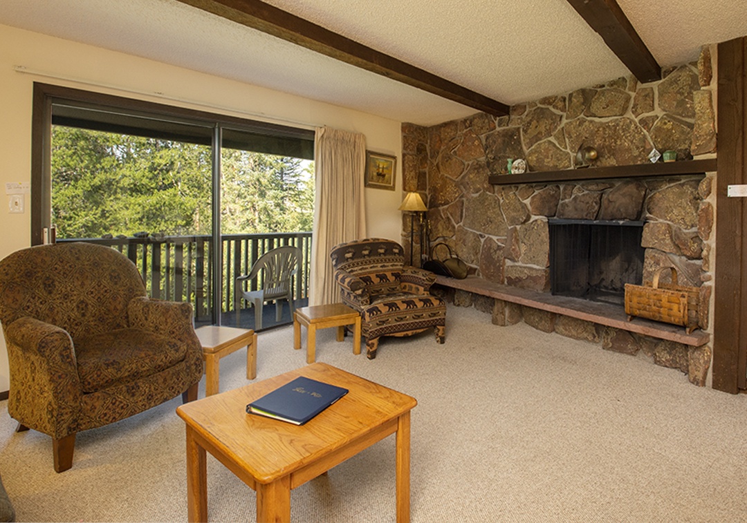 Relax in your cozy living room where exposed beams meet rustic charm, complete with stone fireplace and peaceful forest views from your private balcony.
