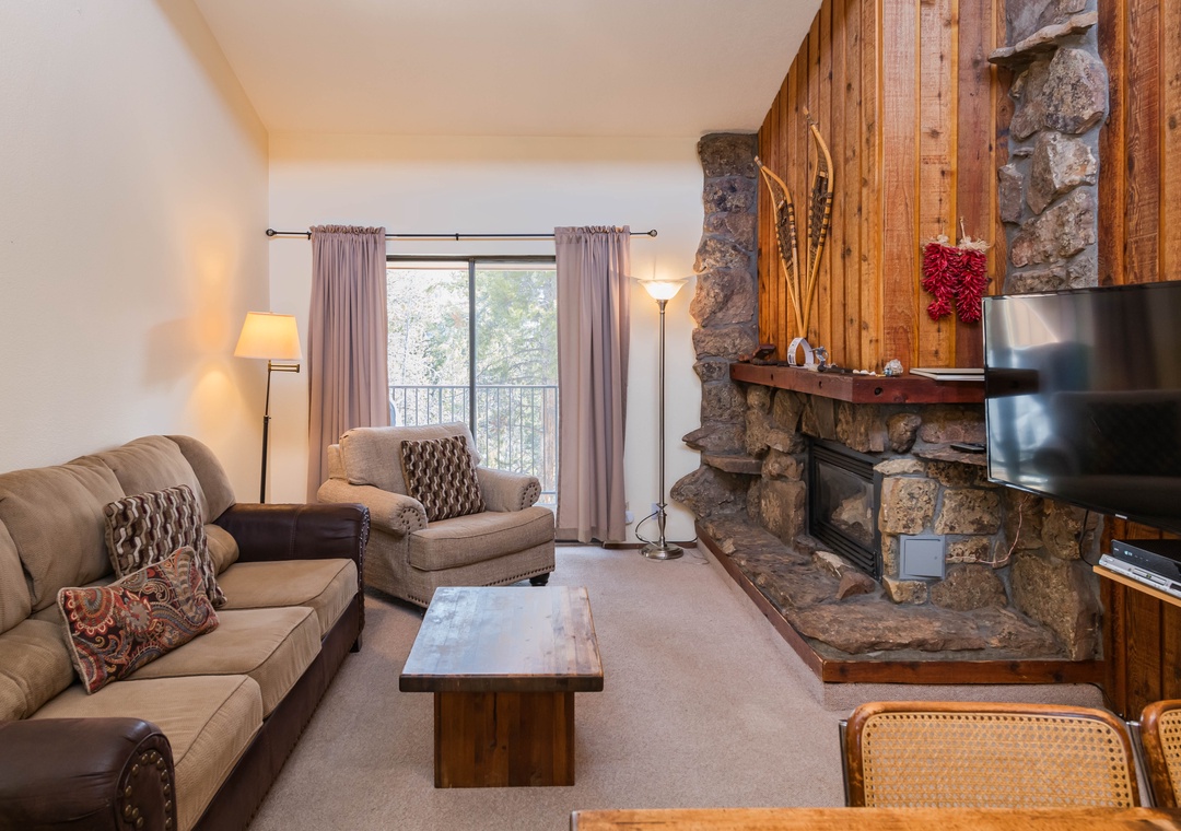 Cozy up by the stone fireplace while you enjoy mountain views from your private balcony in this warm, inviting living space.