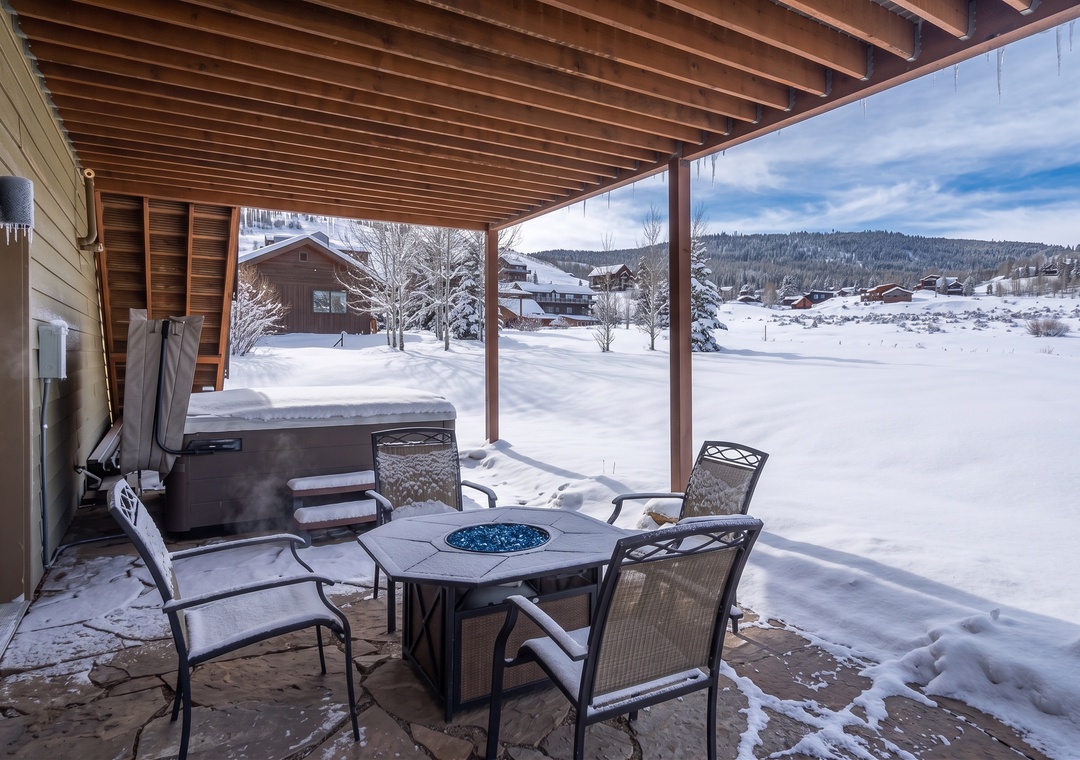 Covered patio with hot tub, fire pit seating, and mountain views—perfect for relaxing after a day of winter adventures.
