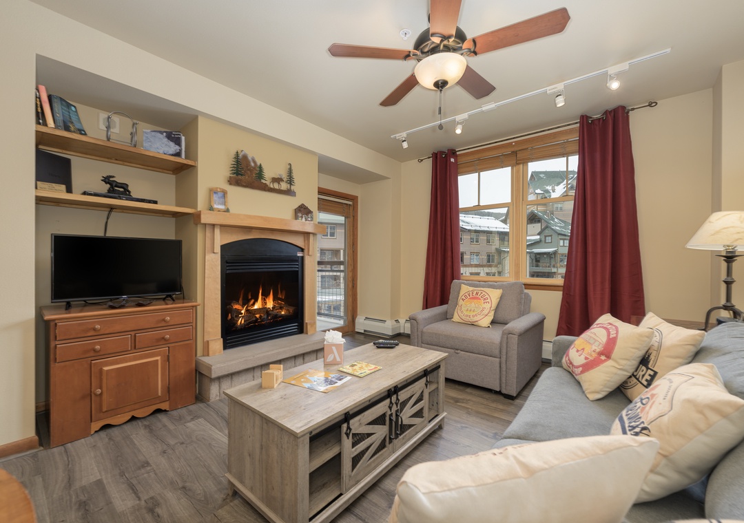 Unwind in your cozy living space with crackling fireplace, plush seating, and mountain views through oversized windows.