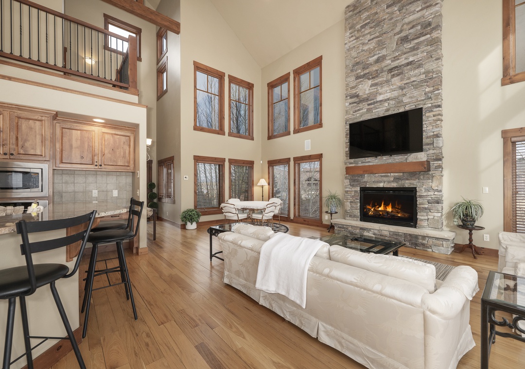 Relax in your spacious living room with soaring ceilings, crackling stone fireplace, and abundant natural light streaming through floor-to-ceiling windows.