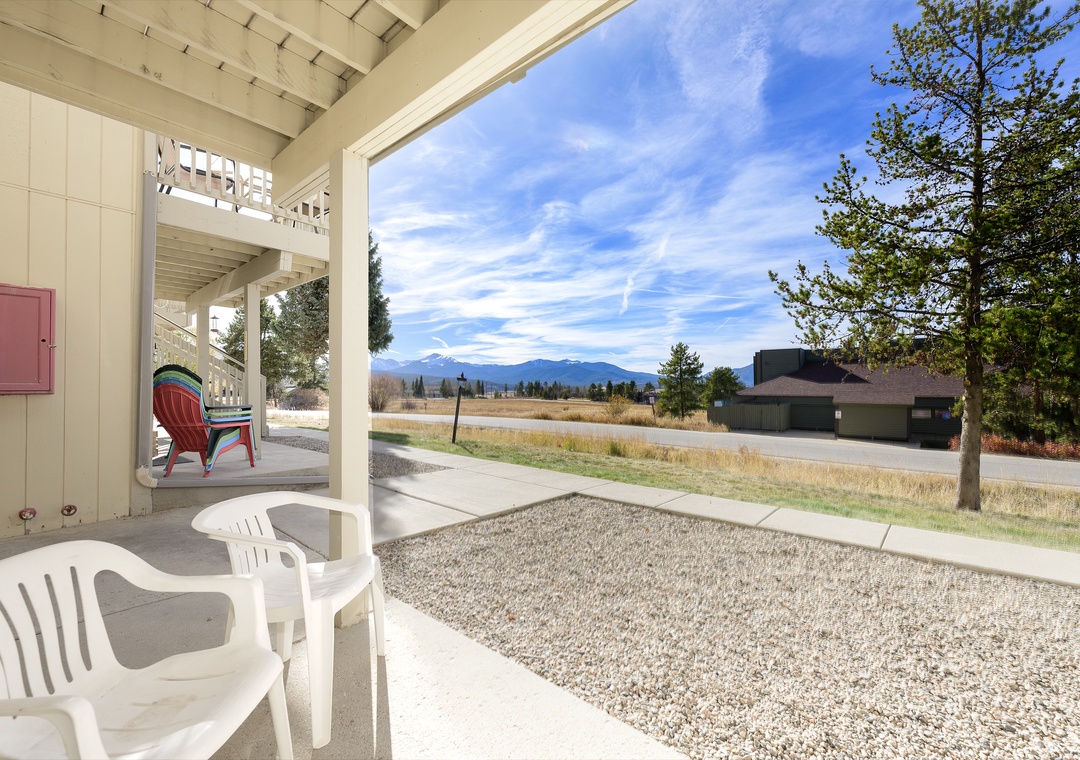 Covered patio with outdoor seating overlooking mountain vistas and open fields in a peaceful residential setting.