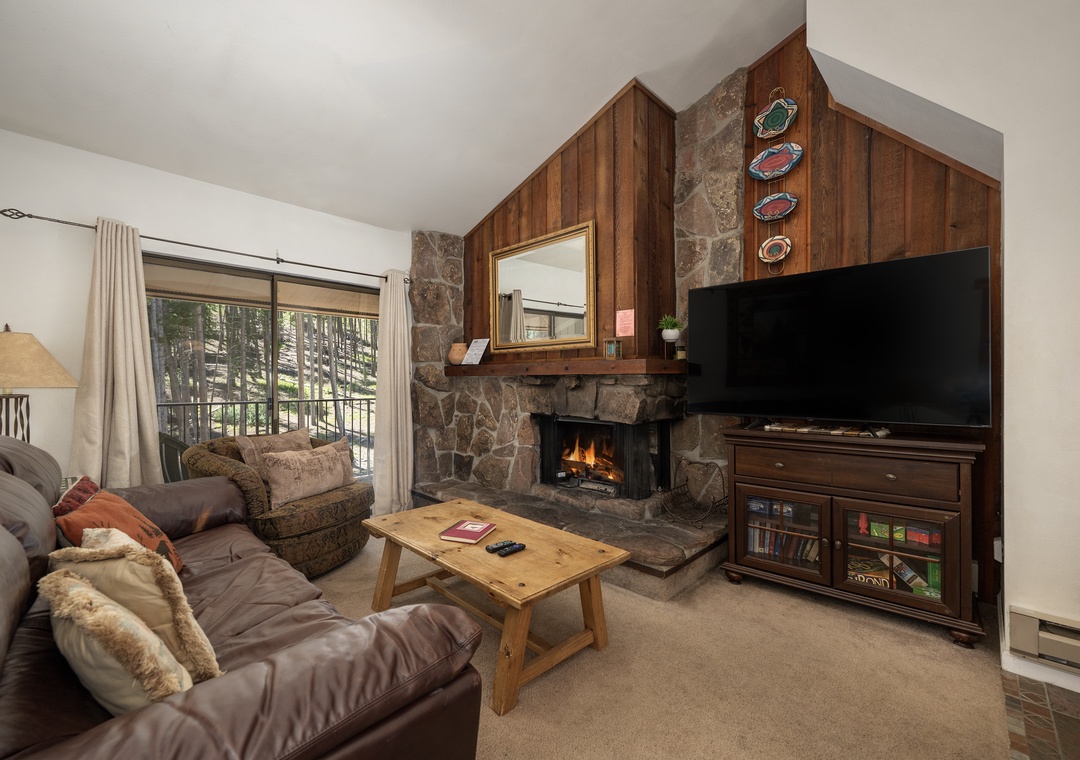Cozy up in your inviting living room featuring a crackling stone fireplace, plush seating, and mountain views through your private balcony.