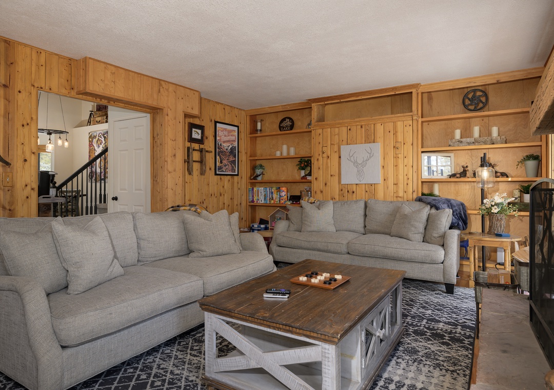 Relax in your cozy living room at 1126 Western Road with warm wood paneling, plush gray sofas, and rustic charm that makes you feel right at home.