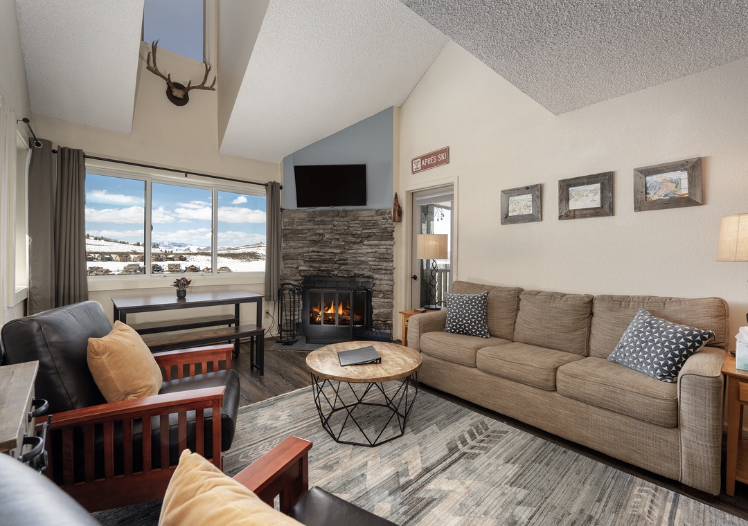 Cozy up by your stone fireplace at Summit Unit 1303 while enjoying mountain vistas through expansive windows in this welcoming living space.