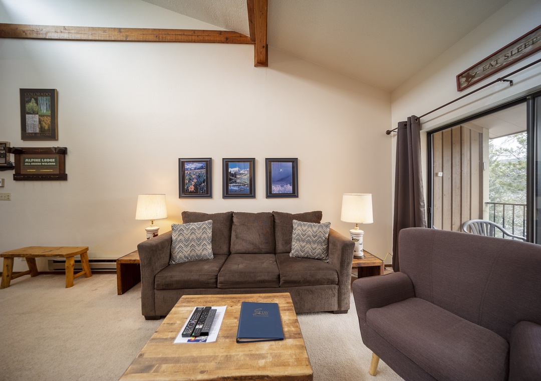 Relax in your cozy living room with exposed wood beams, plush seating, and forest views through the sliding door.