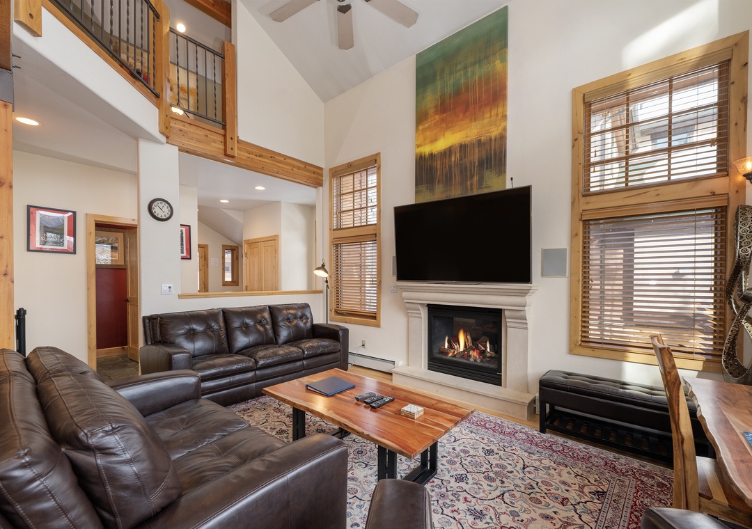 Your spacious living room beckons with plush leather seating, a crackling fireplace, and soaring ceilings that create an airy mountain retreat atmosphere.