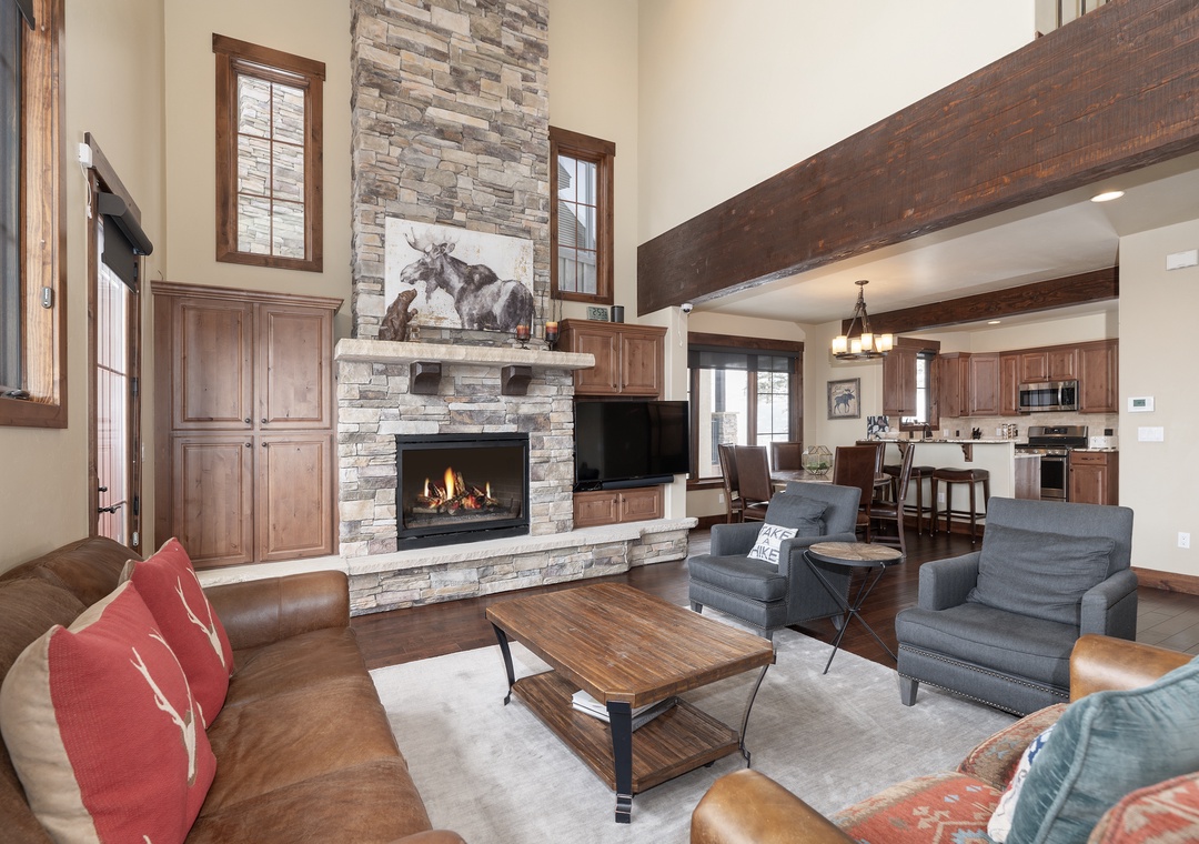 Gather around the crackling stone fireplace in this stunning open-concept space, where rustic beams and warm wood blend seamlessly with your mountain getaway comfort.