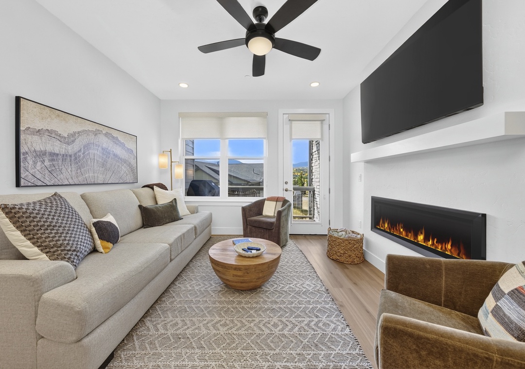 Sink into plush seating as the sleek fireplace casts a warm glow across your retreat. Large windows and a private balcony invite in natural light and mountain air, while the modern ceiling fan keeps you comfortably cool.