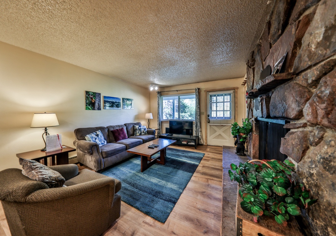 Unwind in your cozy living room with plush seating, warm stone fireplace, and natural light streaming through large windows.