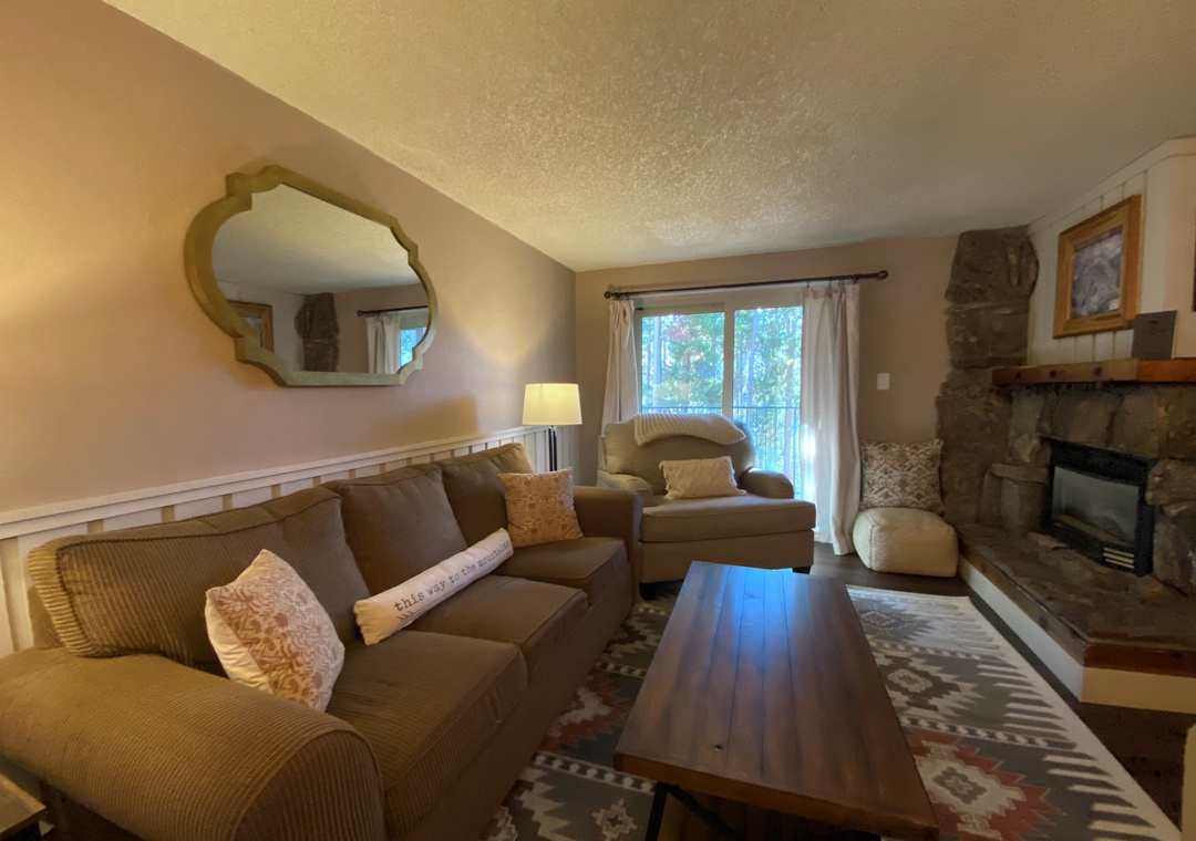 Relax in your cozy living room with plush seating, warm fireplace, and peaceful forest views through sliding doors.