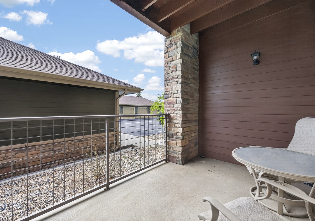 Private covered balcony with seating area overlooking a quiet residential neighborhood. The stone column and wooden ceiling add warmth and charm to this outdoor retreat.